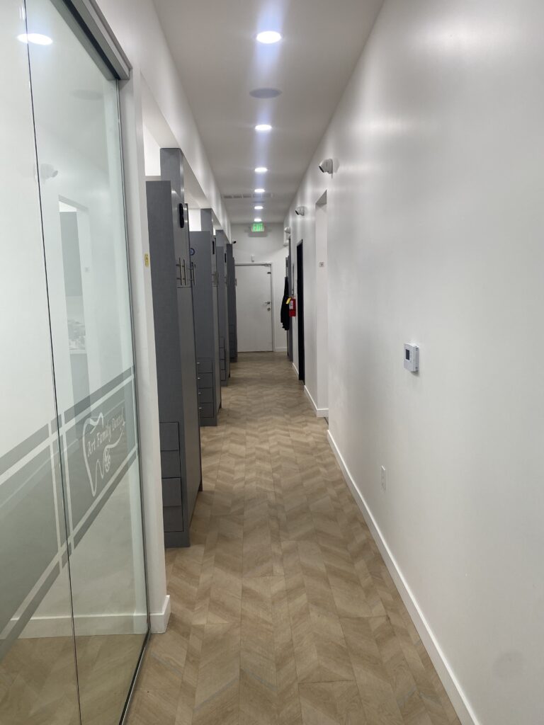 Clean, modern hallway with a wooden herringbone floor and frosted glass doors at Art Family Dental clinic.